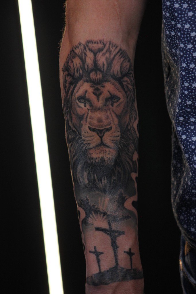 Black and grey realism lion tattoo above three crosses on Golgotha, on an inner forearm