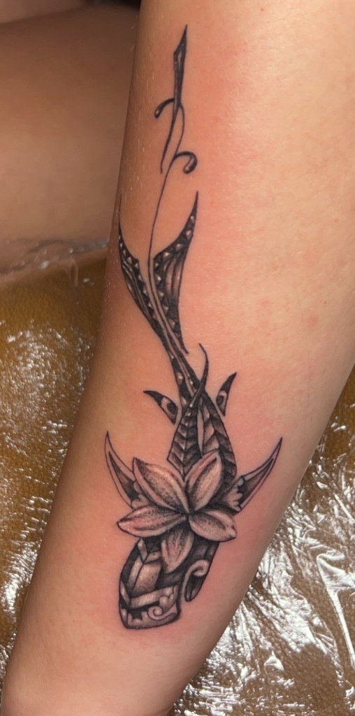 Ornamental tattoo of a lily bloom over patterned neo-tribal blades running up a calf